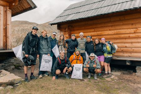 Eine Gruppe Ehrenamtlicher vor einer Holzhütte mit Säcken bewaffnet zum Aufsammeln von Müll bei den CleanUp Days 